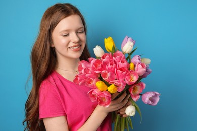 Photo of Beautiful teenage girl with bouquet of tulips on light blue background