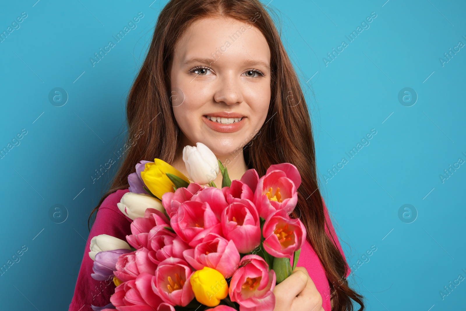 Photo of Beautiful teenage girl with bouquet of tulips on light blue background