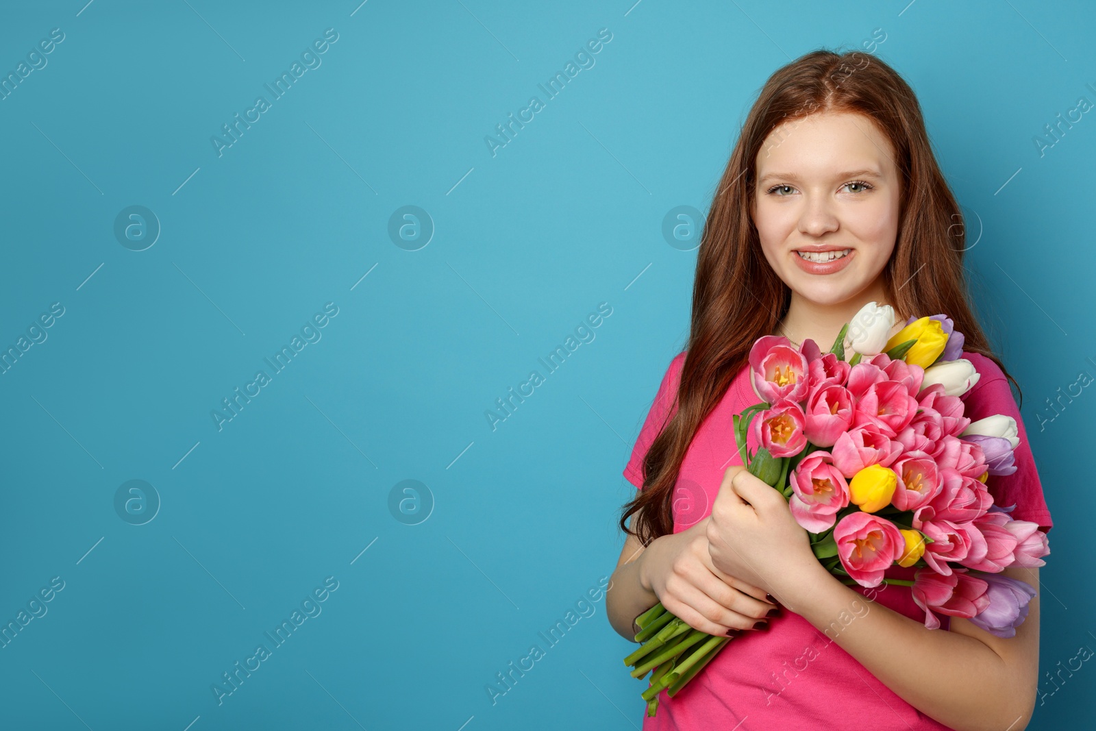 Photo of Beautiful teenage girl with bouquet of tulips on light blue background, space for text