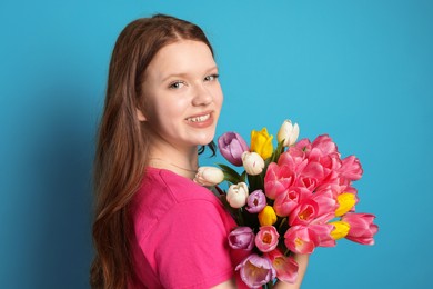 Photo of Beautiful teenage girl with bouquet of tulips on light blue background