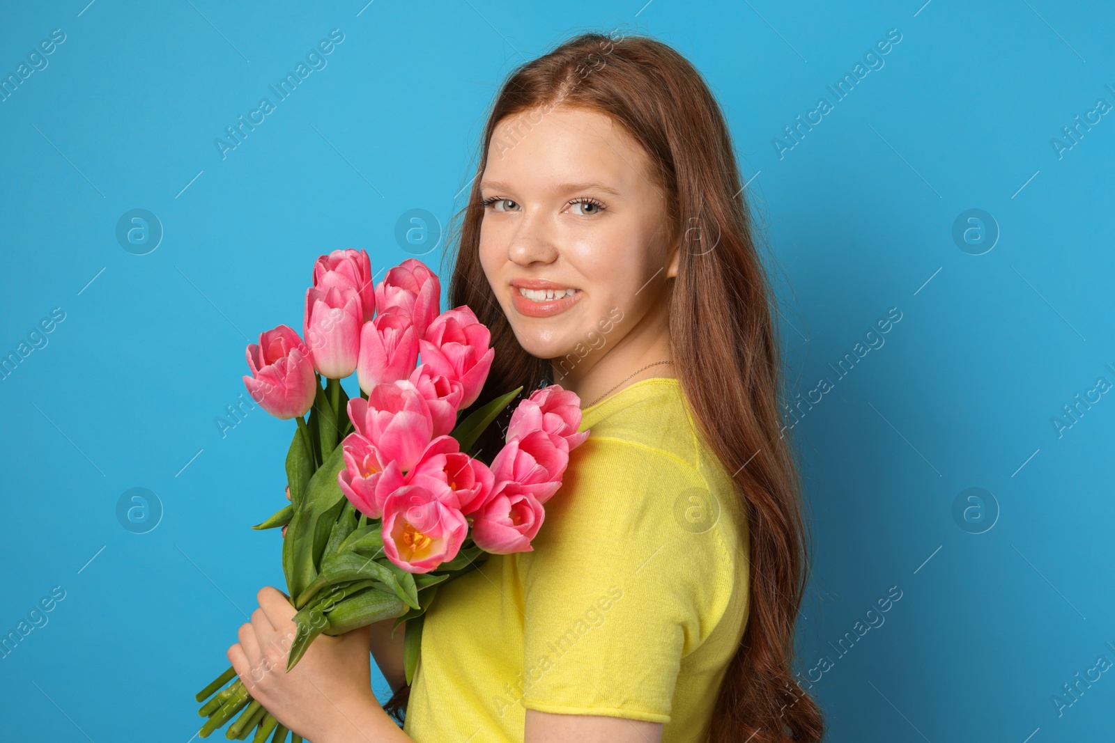 Photo of Beautiful teenage girl with bouquet of tulips on light blue background