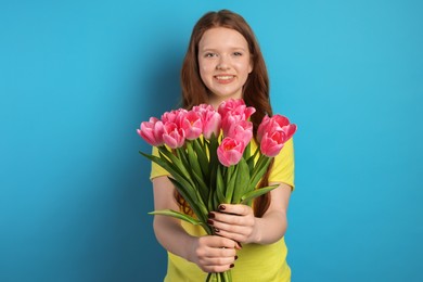 Photo of Beautiful teenage girl with bouquet of tulips on light blue background