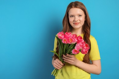 Photo of Beautiful teenage girl with bouquet of tulips on light blue background, space for text