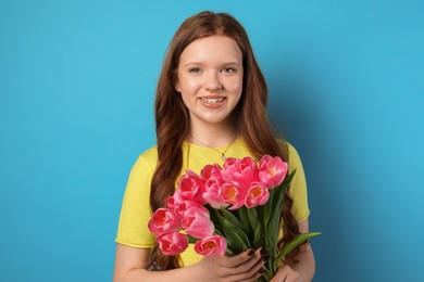 Photo of Beautiful teenage girl with bouquet of tulips on light blue background