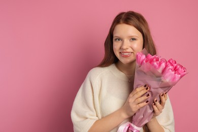 Photo of Beautiful teenage girl with bouquet of tulips on pink background, space for text