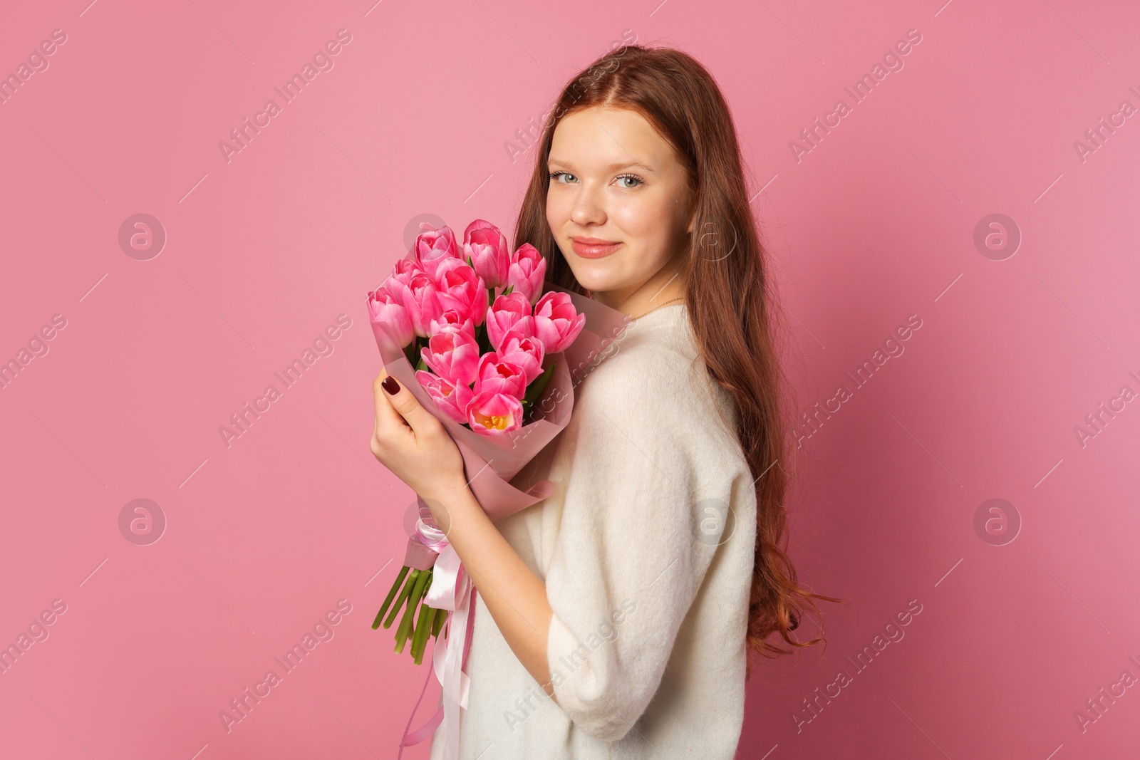 Photo of Beautiful teenage girl with bouquet of tulips on pink background