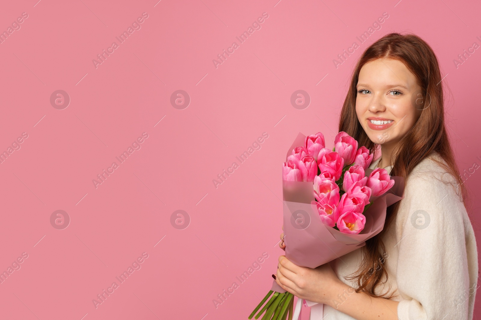 Photo of Beautiful teenage girl with bouquet of tulips on pink background, space for text