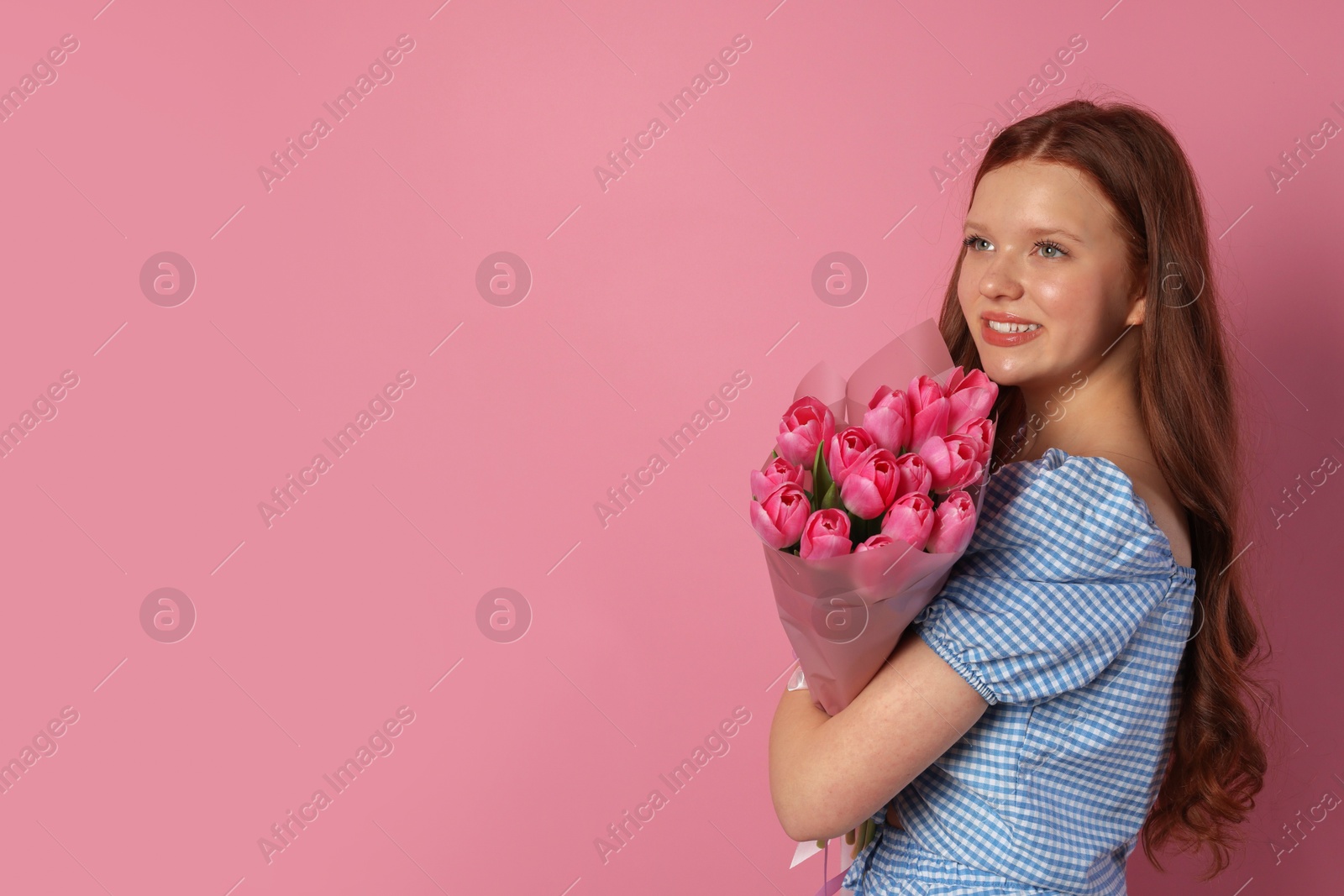 Photo of Beautiful teenage girl with bouquet of tulips on pink background, space for text