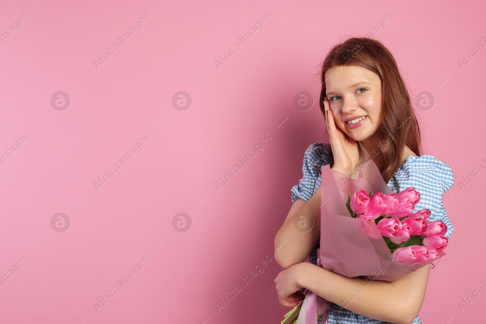 Photo of Beautiful teenage girl with bouquet of tulips on pink background, space for text