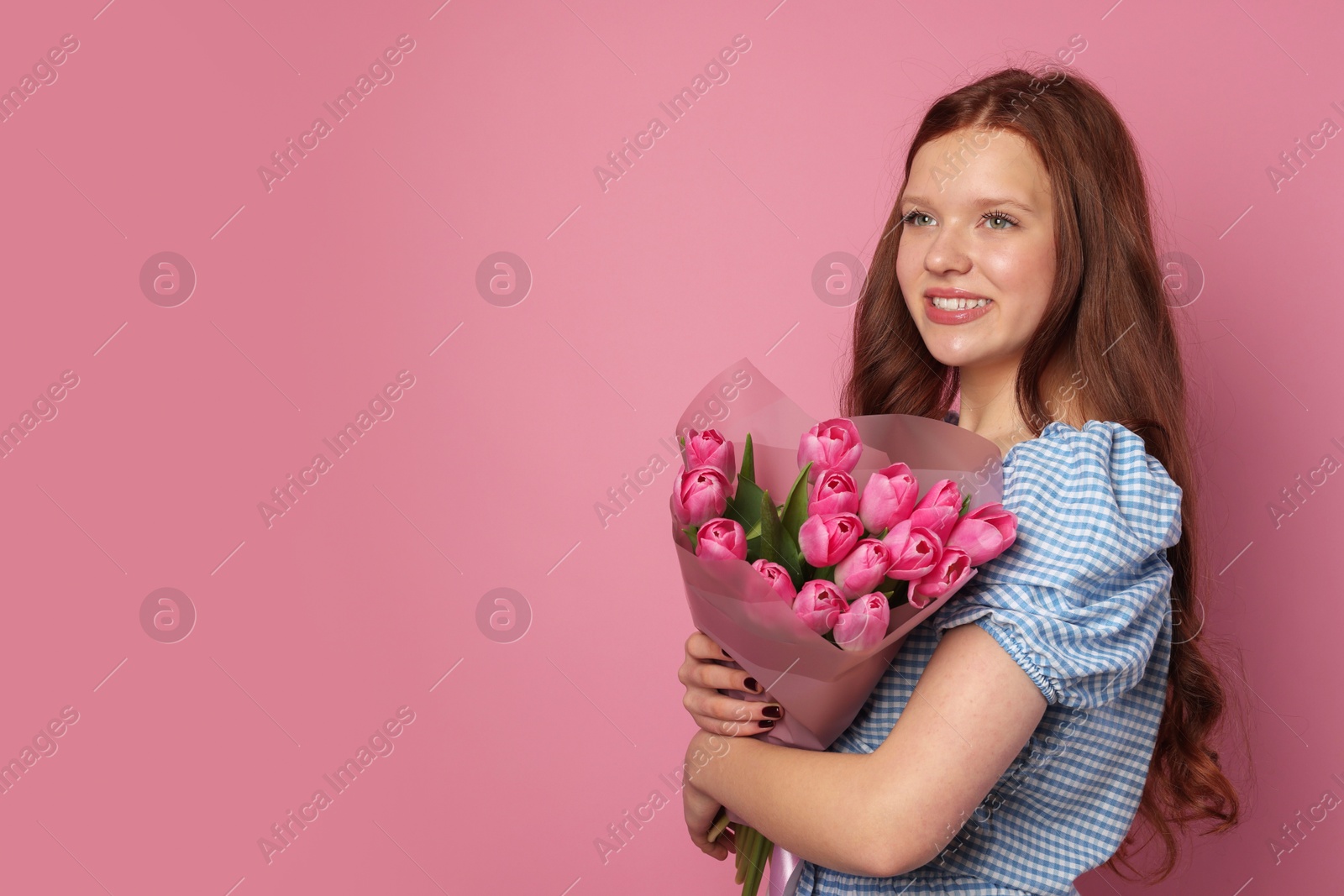 Photo of Beautiful teenage girl with bouquet of tulips on pink background, space for text