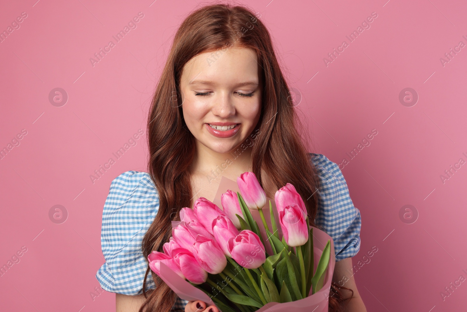 Photo of Beautiful teenage girl with bouquet of tulips on pink background