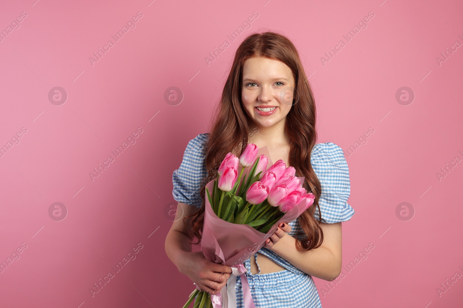 Photo of Beautiful teenage girl with bouquet of tulips on pink background