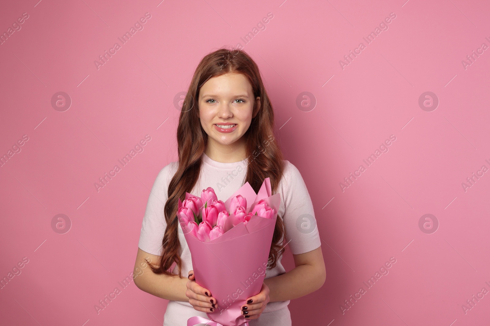 Photo of Beautiful teenage girl with bouquet of tulips on pink background