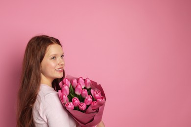 Photo of Beautiful teenage girl with bouquet of tulips on pink background, space for text