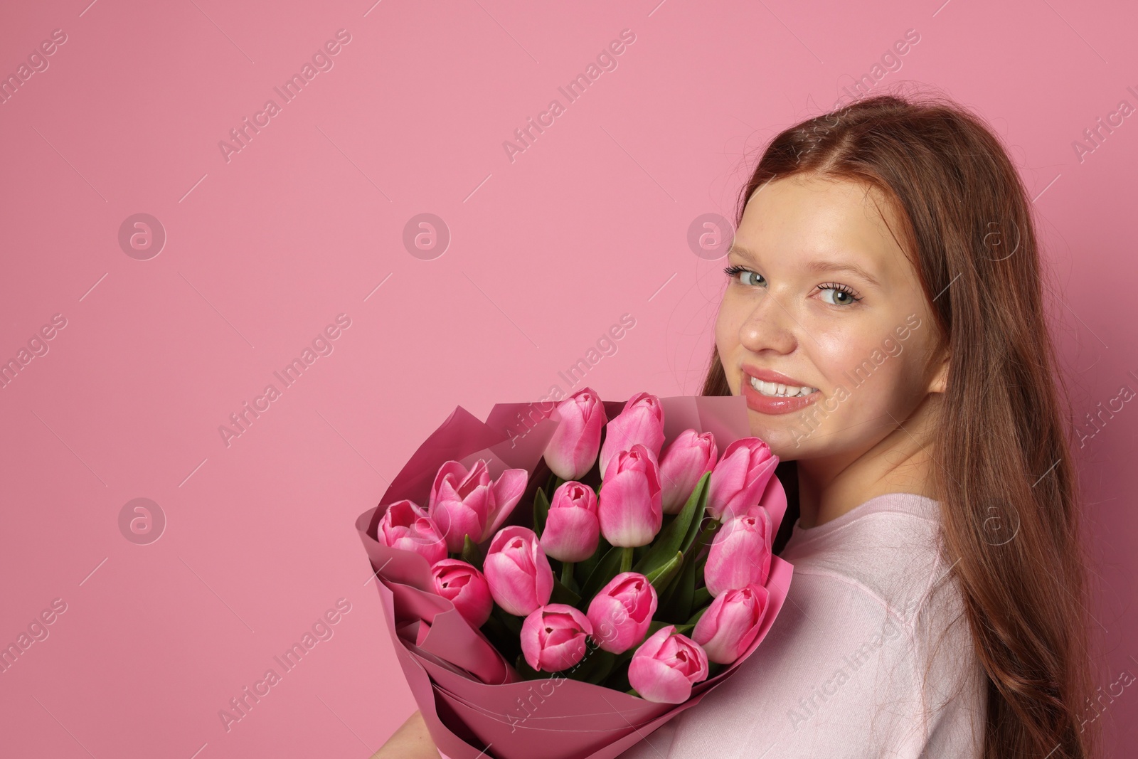 Photo of Beautiful teenage girl with bouquet of tulips on pink background, space for text