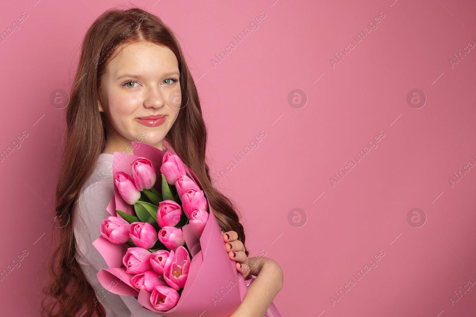 Photo of Beautiful teenage girl with bouquet of tulips on pink background, space for text