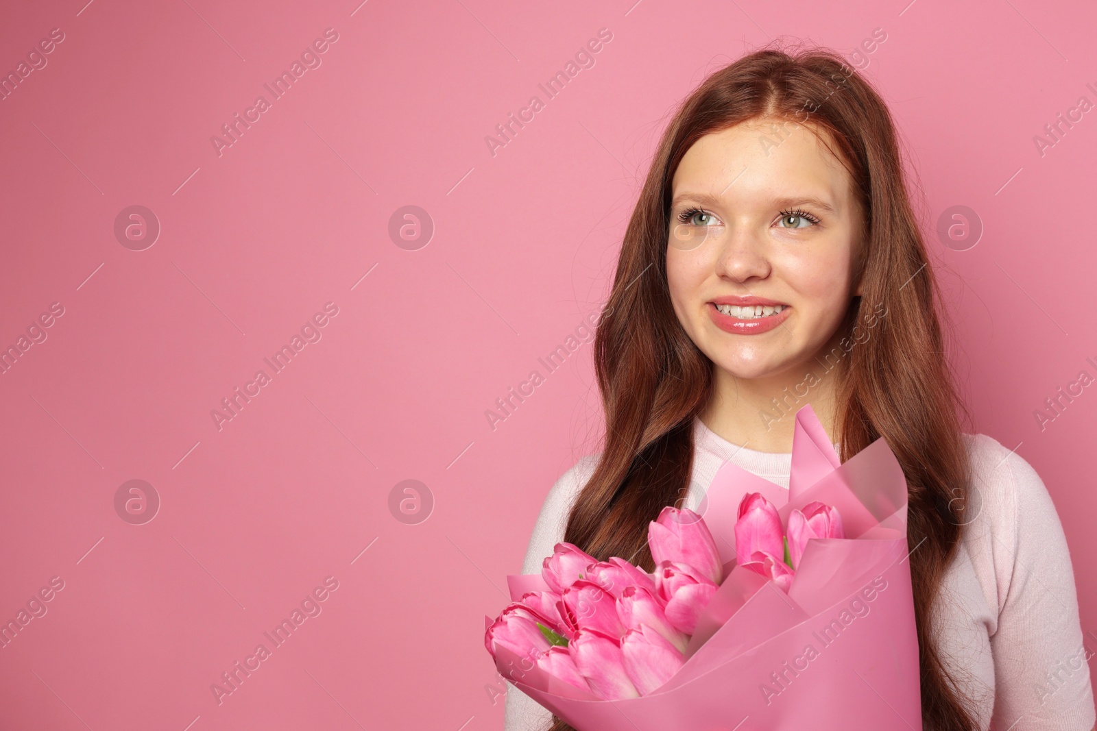 Photo of Beautiful teenage girl with bouquet of tulips on pink background, space for text