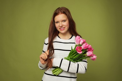 Photo of Beautiful teenage girl with bouquet of tulips on olive background