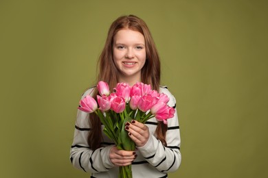 Photo of Beautiful teenage girl with bouquet of tulips on olive background