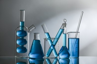 Photo of Laboratory glassware with blue liquid on mirror surface against grey background