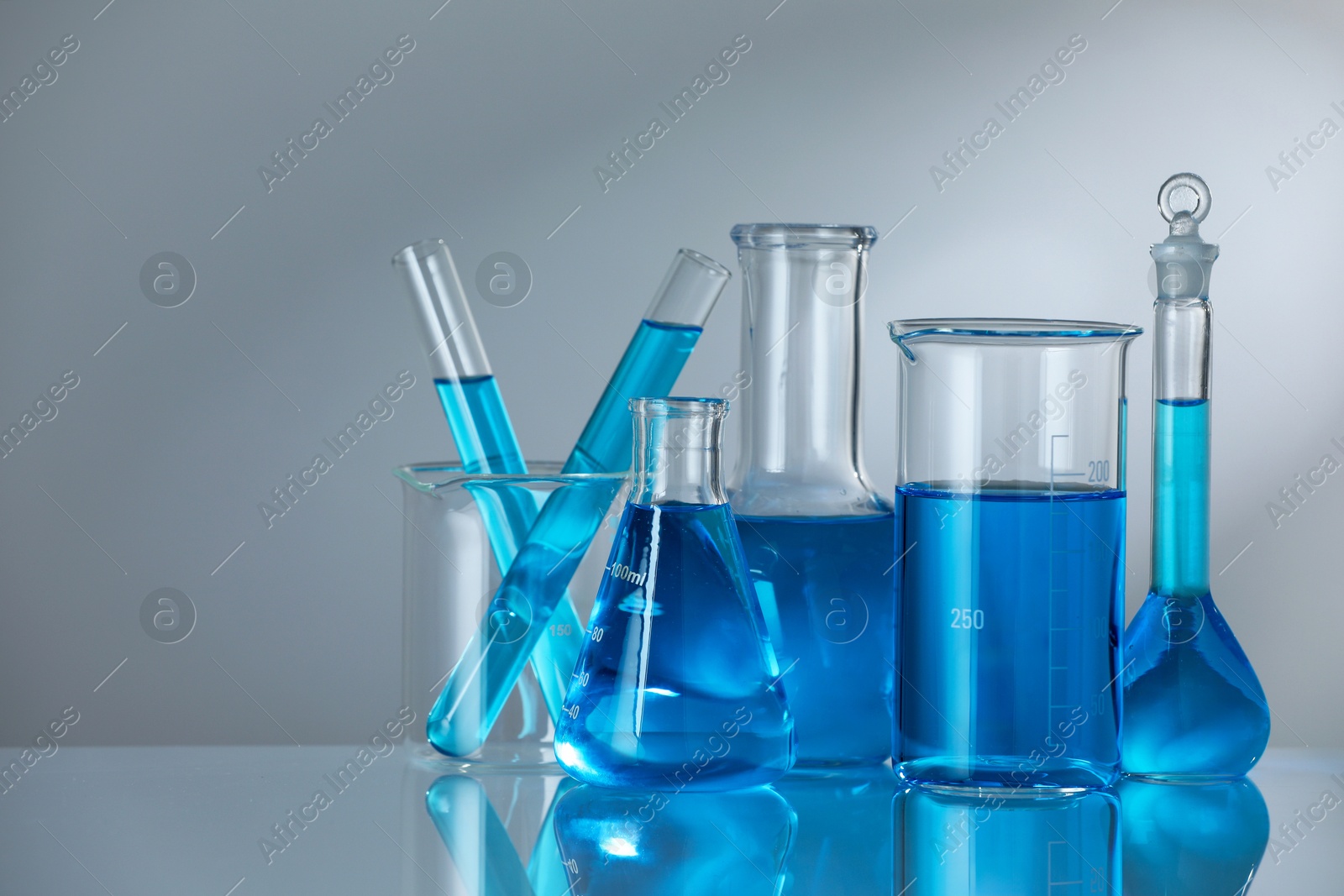 Photo of Laboratory glassware with blue liquid on mirror surface against grey background