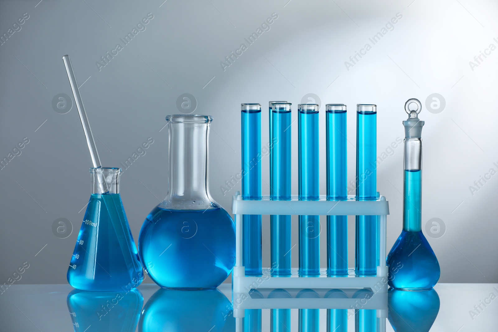 Photo of Laboratory glassware with blue liquid on mirror surface against grey background