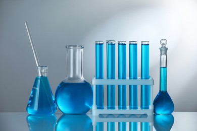 Photo of Laboratory glassware with blue liquid on mirror surface against grey background