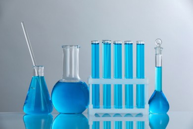 Photo of Laboratory glassware with blue liquid on mirror surface against grey background