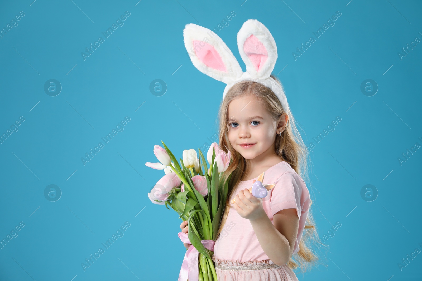 Photo of Cute little girl with bunny ears and spring flowers on light blue background. Easter celebration