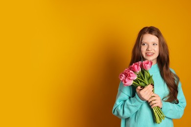 Photo of Beautiful teenage girl with bouquet of tulips on orange background, space for text