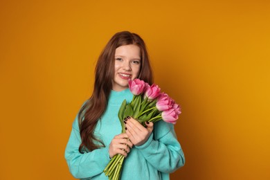 Photo of Beautiful teenage girl with bouquet of tulips on orange background