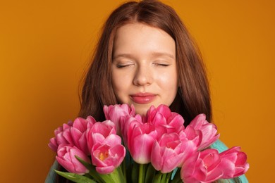 Photo of Beautiful teenage girl with bouquet of tulips on orange background, closeup