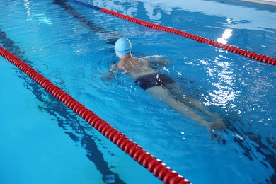 Photo of Young man in cap and swimwear swimming in pool indoors