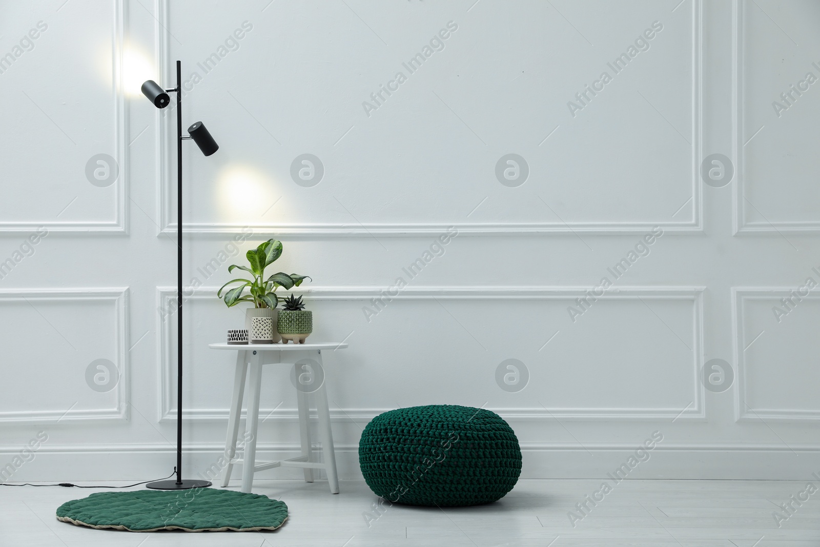 Photo of Stylish room interior with pouf, lamp and houseplants. Space for text