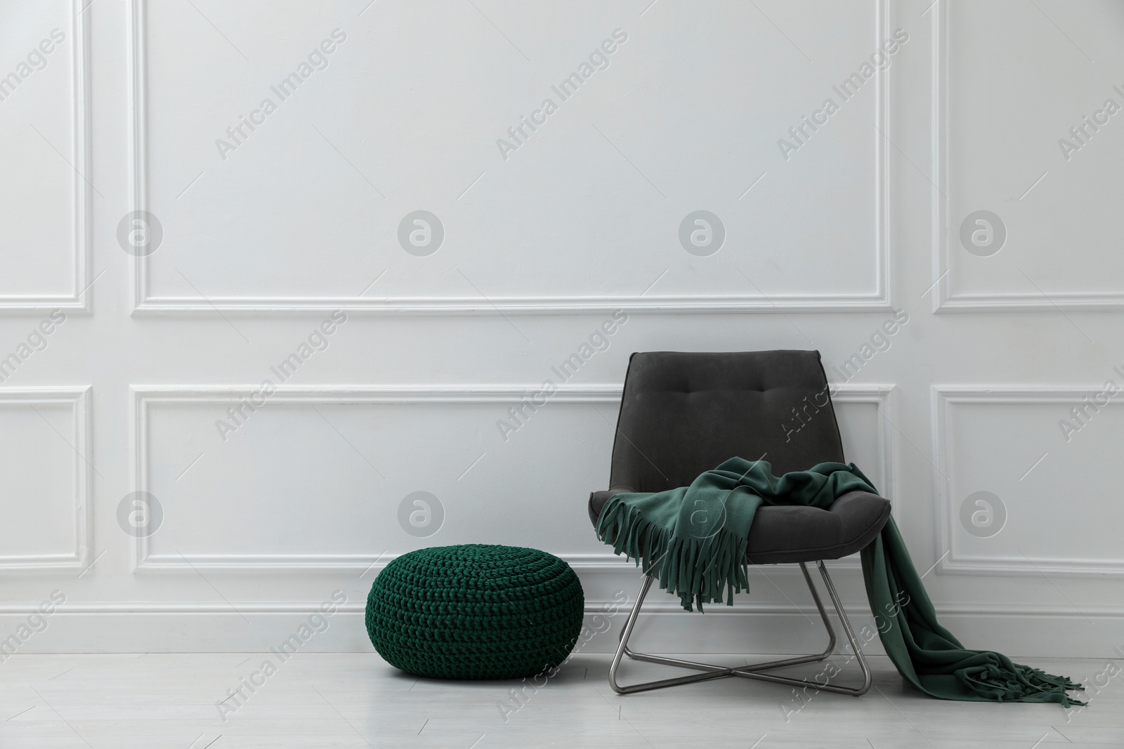 Photo of Knitted pouf and chair with plaid near white wall indoors. Space for text