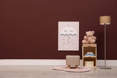 Photo of Stylish beige ottoman, shelving unit with toy bear and lamp in room. Space for text