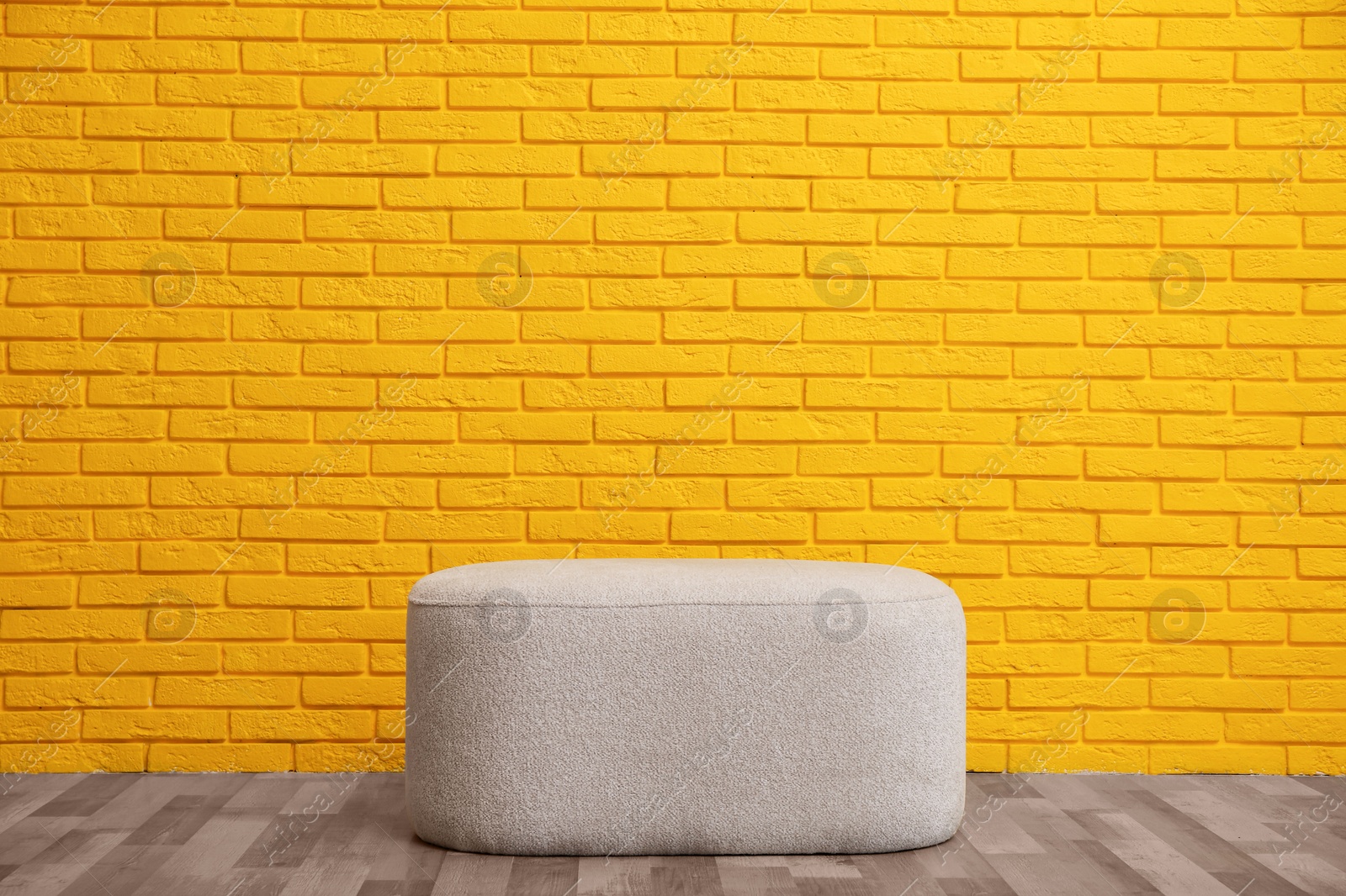 Photo of Stylish comfortable pouf near yellow brick wall. Interior design