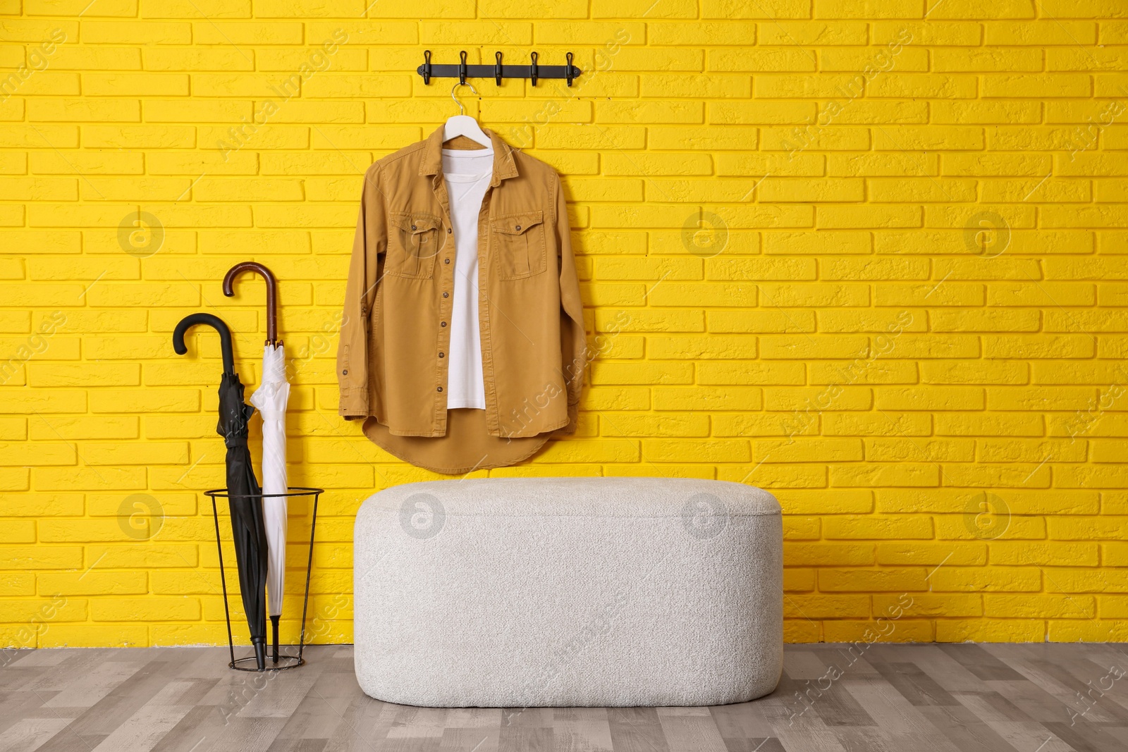 Photo of Stylish comfortable pouf near yellow brick wall in hallway