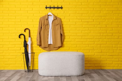 Photo of Stylish comfortable pouf near yellow brick wall in hallway