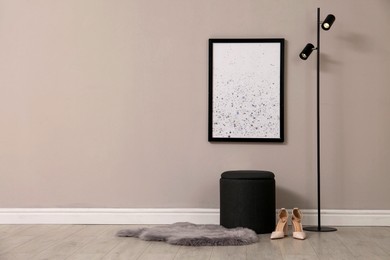 Photo of Stylish pouf, lamp, shoes and faux fur near beige wall indoors. Space for text