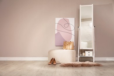 Photo of Stylish pouf and mirror near beige wall indoors. Space for text