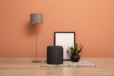 Photo of Comfortable pouf, plant, lamp and picture near pale pink wall indoors