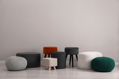 Photo of Different stylish poufs and ottomans near light grey wall