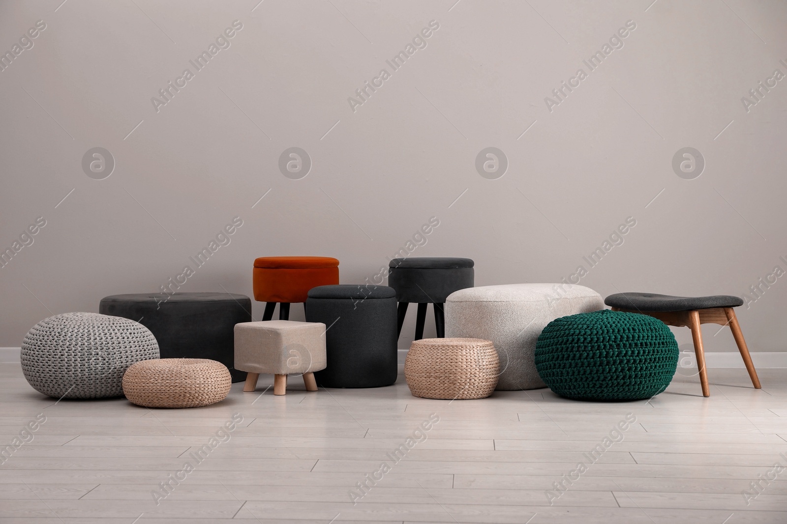 Photo of Different stylish poufs and ottomans near light grey wall