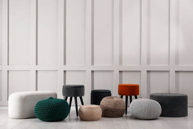 Photo of Different stylish poufs and ottomans near light wall