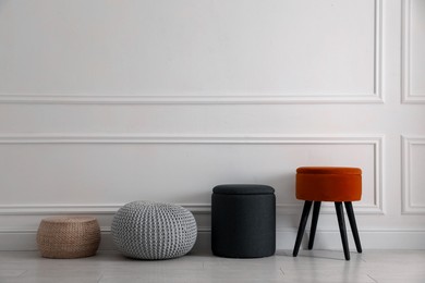 Photo of Different stylish poufs and ottomans near light wall