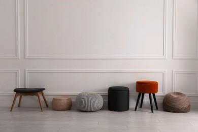 Photo of Different stylish poufs and ottomans near light wall