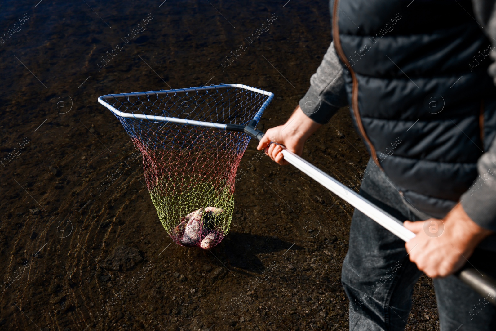 Photo of Fisherman holding fishing net with catch at riverside, closeup