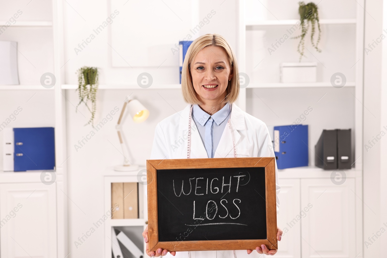 Photo of Happy nutritionist holding small blackboard with words Weight loss in clinic