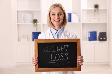 Photo of Happy nutritionist holding small blackboard with words Weight loss in clinic